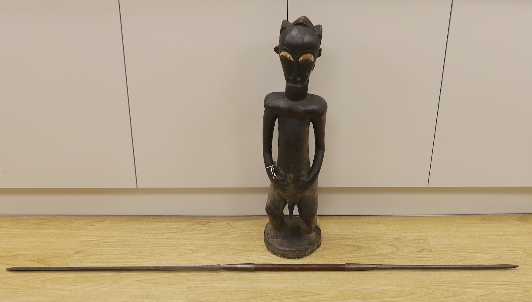 An African Baoule crouched tribal figure, together with a spear, 156cm long